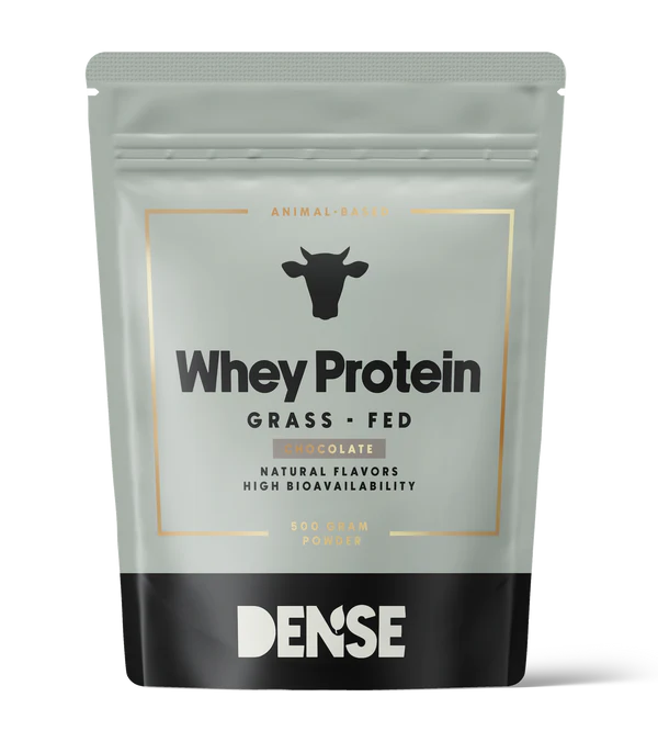 DENSE Heraproteiini Suklaa; hopeanvärinen ja musta mattapintainen pystypussi, suorakulmainen muodoltaan, esittää selkeää painettua tekstiä Whey Protein Grass-Fed ja sanan DENSE lihavan lehmäääriviivan alla; etuetiketissä yksinkertaista lohkotypografiaa, korostaen suklaan makua, luonnollisia makuja, korkeaa biosaatavuutta ja laiduntavista lähteistä peräisin olevia ainesosia; tuote esillä yksivärista taustaa vasten studiotyylisessä kuvassa.