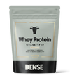 DENSE Heraproteiini Vanilja; harmaa ja musta mattapintainen pussi suorakulmaisella muodolla, merkissä Dense yläreunassa, teksti kertoo Whey Protein, Grass-Fed, Vanilla; yksinkertainen lehmäkuvake tekstin alla; pussi korostaa luonnollisia makuja ja korkeaa biosaatavuutta laiduntavista lähteistä groteskifontilla; tuote seisoo pystyssä vaaleaa taustaa vasten, ei ihmisiä tai käsiä näkyvissä.