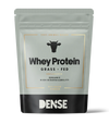 DENSE Luomu Heraproteiini Maustamaton; hopeanvärinen ja musta pussi, merkitty Whey Protein Grass Fed, lehmäkuvake, tekstissä kerrotaan maustamattomasta, luomulaadusta ja korkeasta biosaatavuudesta; DENSE-merkki lihavalla groteskifontilla; pakkauksessa ilmoitetaan 500 g proteiinijauhetta; mattapintainen, uudelleensuljettava, suorakulmainen pystypussi; tausta neutraali ja tasainen, ei ihmisiä tai esineitä näkyvissä.