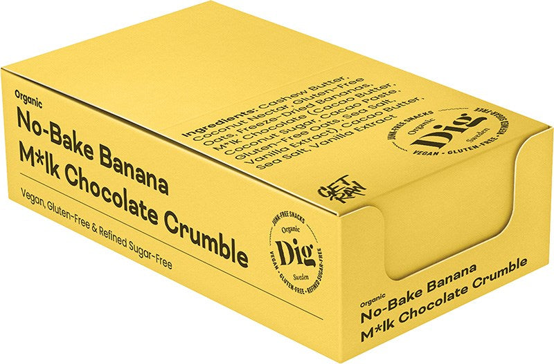 Dig Luomu Banaani-Suklaacrumble; keltainen suorakulmainen laatikko mattapinnalla, merkitty No-Bake Banana M*lk Chocolate Crumble, kuvakkeineen vegaanisuudesta, gluteenittomuudesta ja puhdistetusta sokerista vapaasta koostumuksesta; luettava ainesosaluettelo ja brändäys etupuolella; laatikossa kuva paistamattomasta jälkiruoasta; ei ihmisiä näkyvissä; tausta vaalea pehmeällä valaistuksella tuotekuva-asetelmassa.