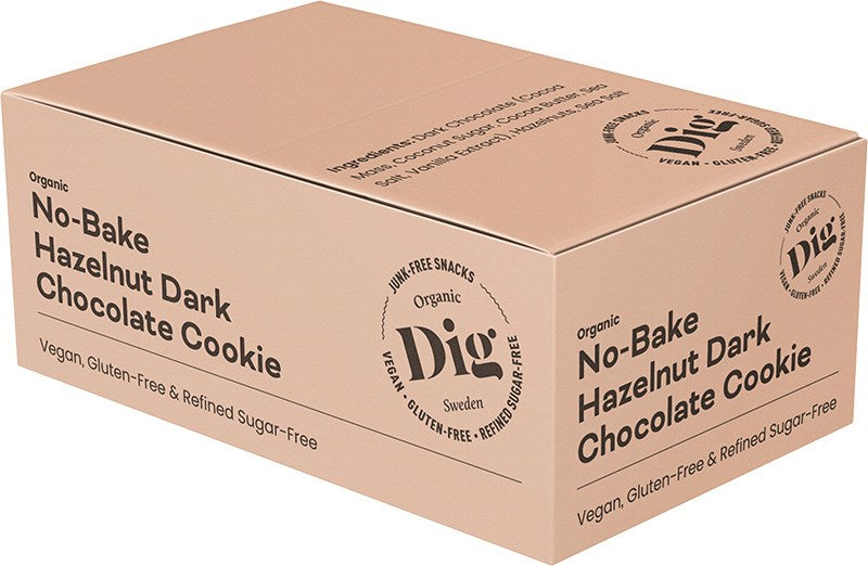 Dig Luomu Hasselpähkinä-Tumma Suklaakeksi; beige laatikko, merkitty No-Bake Hazelnut Dark Chocolate Cookie by Dig, merkitty luomuksi, vegaaniseksi, gluteenittomaksi ja puhdistetusta sokerista vapaaksi; pakkaus on suorakulmainen pyöristetyin reunoin ja mattapinnalla; lihavaa mustaa tekstiä käytetään tuotetiedoissa; pinta vaikuttaa sileältä; ei ihmisiä tai käsiä näkyvissä; tausta yksivärinen, lähikuva tuotteesta.