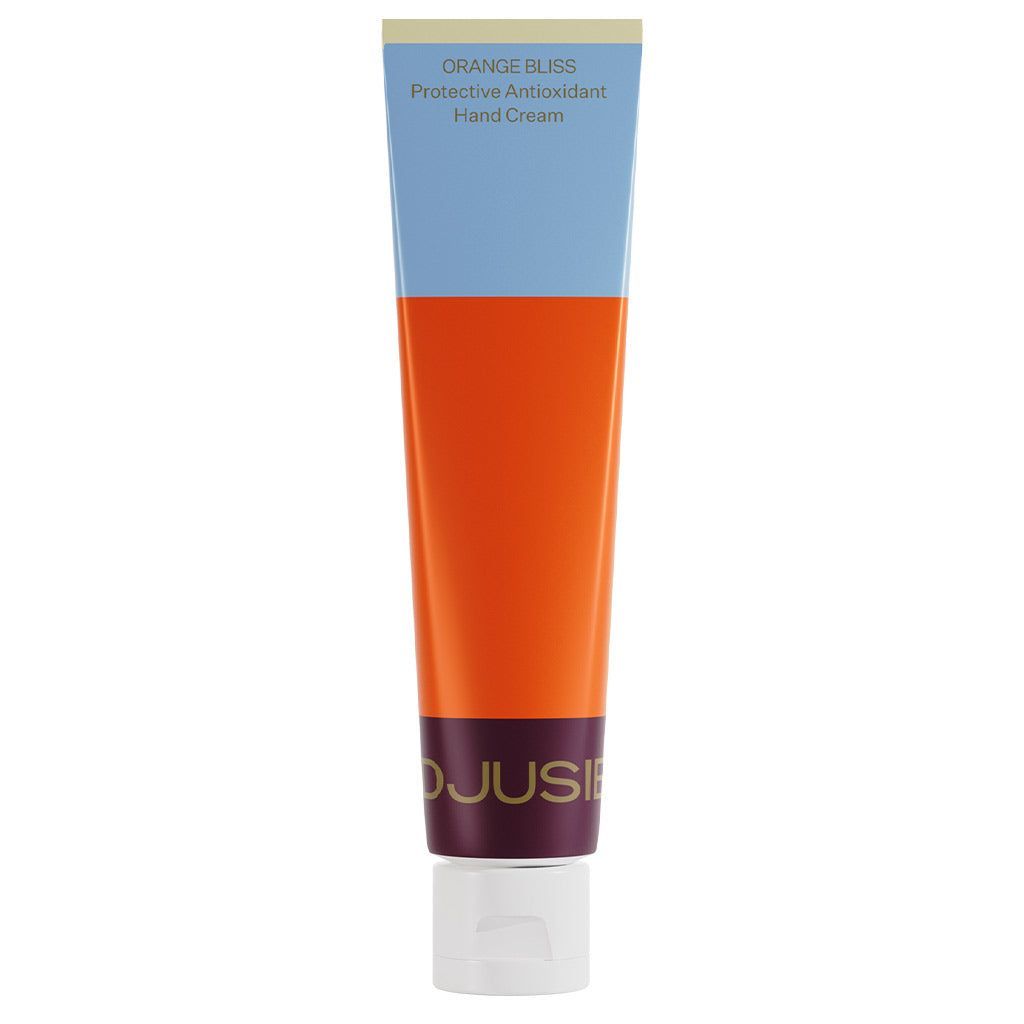 Djusie Orange Bliss Käsivoide; tuubi käsivoiteelle tekstillä "ORANGE BLISS Protective Antioxidant Hand Cream" pystyssä valkoisella korkilla; pakkauksessa eloisia sinisiä, oransseja ja viininpunaisia väripalikoita mattapinnalla; tuubi lieriön muotoinen ja taipuisaa materiaalia; etikettityyppografia lihavoitua sans-serifiä eri kokoina; ei käsiä tai ihmisiä; tausta yksinkertainen.