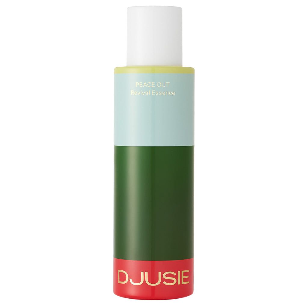 A cylindrical bottle with a red base, dark green middle, light blue top, and white cap is labeled DJUSIE and PEACE OUT Revival Essence, featuring an essence that revitalizes your skin. The surface is glossy plastic. Sans-serif, bold white text appears on the bottle. Background is plain white with no people or hands. Straight-on product shot.