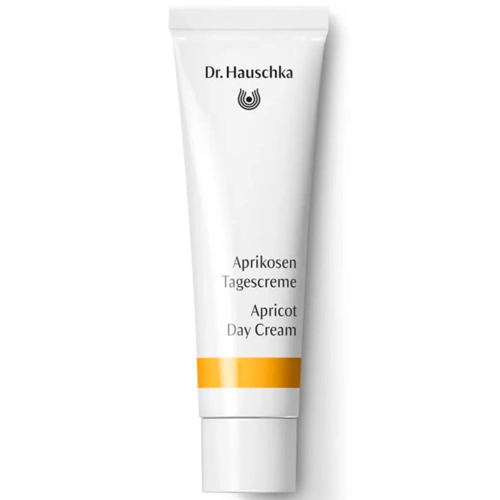 Dr. Hauschka Aprikoosivoide; valkoinen tuubi Dr. Hauschka Apricot Day Cream -tuotetta uudistavine mustine ja oransseine teksteineen sekä keltainen raita tyvellä; tuubi lieriömäinen mattapinnalla ja sileä valkoinen korkki; pakkauksen teksti tikkukirjasimella eri kokoina; tuote pystyssä saumattomalla, yksivärisellä valkoisella taustalla; ei ihmisiä tai käsiä kuvassa.