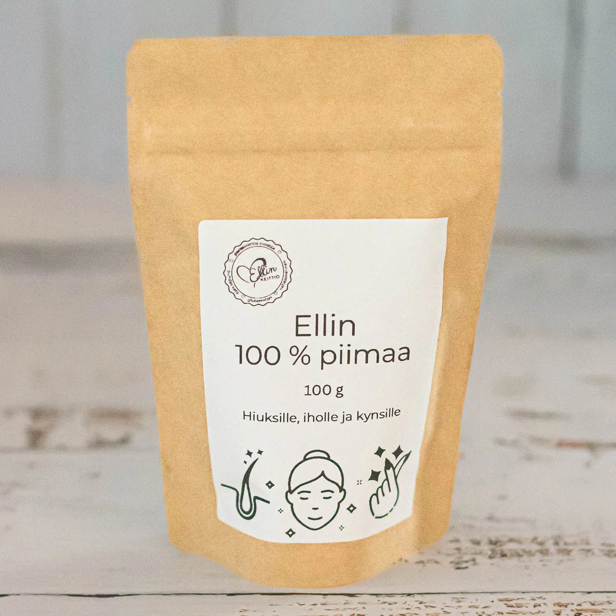 Ellin 100 % Piimaa; ruskea uudelleensuljettava pussi mattapintaisesta materiaalista, suorakulmainen; etiketissä lukee selkeällä groteskilla "Ellin 100% piimaa 100g"; pussissa painokuvia hiuksista, kasvon profiilista ja kynsistä; ei ihmisiä tai käsiä näkyvissä; tausta neutraali, kuva otettu suoraan edestä tasaisessa valaistuksessa.