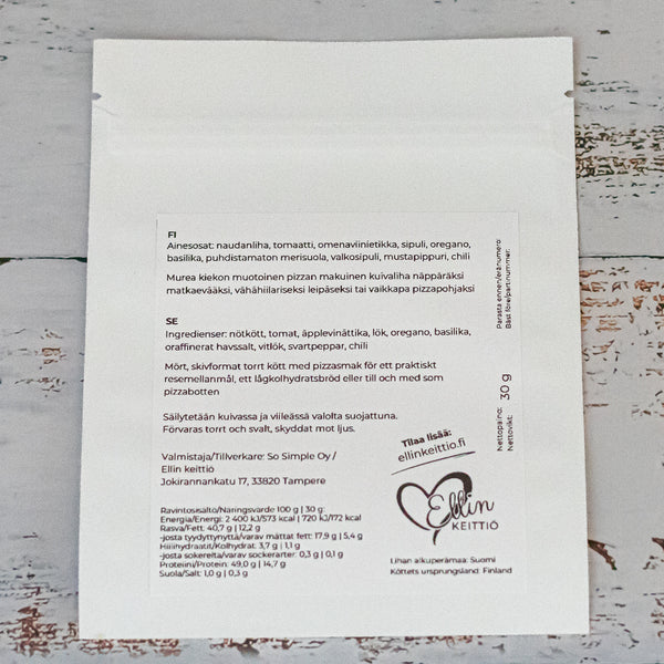 Ellin Lihakiekko Pizzamausteinen; valkoinen elintarvikepussi valmistusohjeineen ja ainesosineen suomeksi ja ruotsiksi rustiikkisella, valkoiseksi maalatulla puupinnalla; mattapintainen pakkaus suorakaiteen muotoinen, painetussa etiketissä näkyvää tikkukirjasinta, Ellin Keittiö -logo, sydänsymboli ja yrityksen osoite; ei ihmisiä tai käsiä näkyvissä; keskikokoinen kuva neutraalissa valaistuksessa.