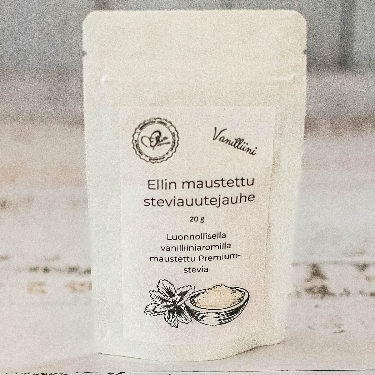 Ellin Vanilliinistevia; valkoinen pussi, jossa lukee Ellin maustettu steviauuttejauhe, kuvituksena steviakasvi ja kulhollinen jauhetta; pakkaus vaikuttaa mattapintaiselta, suorat saumat ja kuumasaumatut reunat; etiketin teksti on lihavaa, modernia groteskia; etiketissä korostetaan luonnollista vaniljan makua ja Premium-steviauutetta; kuvattu yksiväristä taustaa vasten, ei ihmisiä tai käsiä näkyvissä.