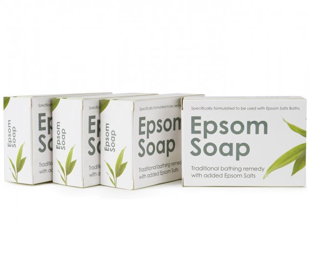 Epsom Suolasaippua; neljä Epsom Soap -saippuapakkausta vihrein lehtikuvioin rivissä; pakkaus suorakaiteen muotoinen mattapinnalla, pääosin valkoinen ja vihreä väritys; etuosassa etiketti groteskifontilla: Epsom Soap, traditional bathing remedy with added magnesium-rich Epsom Salts; ei ihmisiä tai käsiä; vaalea tausta, tavanomainen tuotekuvakulma.