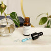 Evolve Blue Velvet Ceramide Serum; pieni ruskea apteekkityylinen pullo etiketillä avattuna marmoripinnalla, vieressä sinistä seerumia sisältävä tiputin; taustalla pyöreä lasimaljakko lehtevine kasveineen; lieriön muotoinen, läpinäkymätöntä meripihkanvärisen lasia mattapintaisena, valkoinen suorakulmainen etiketti groteskitekstillä; tiputin mustalla yläosalla ja kirkkaalla varrella; ei ihmisiä tai käsiä; pehmeästi valaistu marmoripinta.
