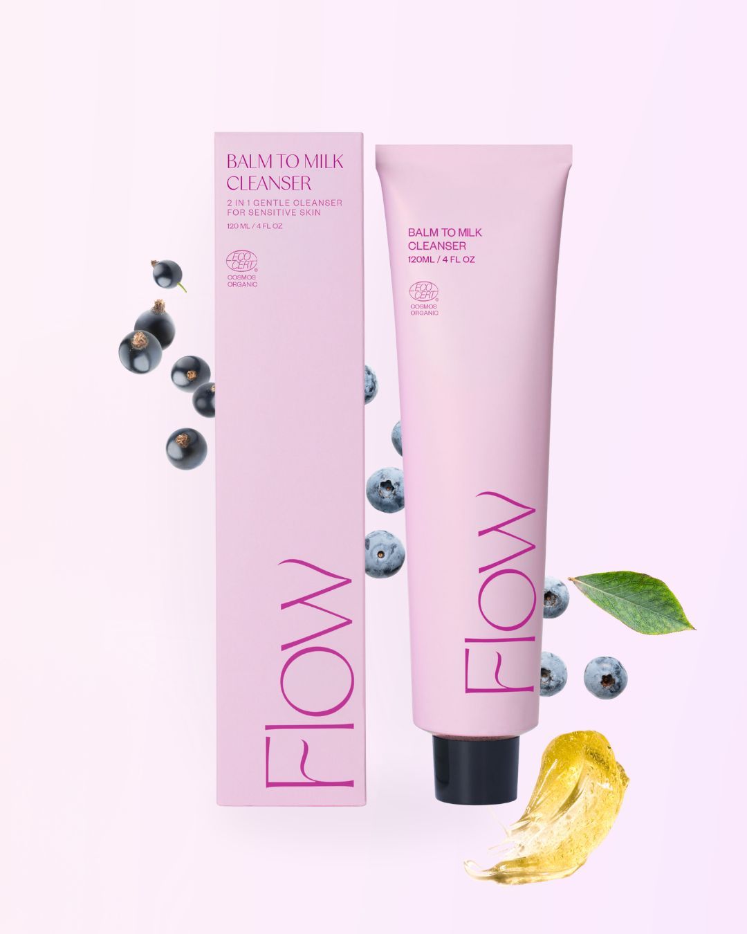 FLOW Cosmetics Balm to Milk Puhdistusvoide: pinkki tuubi ja yhteensopiva rasia tekstillä "Flow Balm to Milk Cleanser" seisovat pystyssä mustaherukoiden, mustikoiden, vihreän lehden ja keltaisen balsamiraidan ympäröiminä vaaleanpinkillä pohjalla; pakkaus on mattapintainen, tuubi pehmeää muovia ja rasia suorakulmainen kartonkia; yksinkertainen valkoinen teksti tuotemerkinnässä; ei ihmisiä tai käsiä näkyvissä, kuva on ylhäältä otettu asetelma.