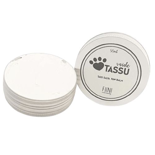 Fiini Naturally Tassuvoide; pieni pyöreä hopeanvärinen purkki mattapintaisena, kannessa tassunjälkikuvake ja teksti "Voide TASSU", sisältää 50 ml hoitavaa tassuvoidetta; avoin purkki paljastaa valkoisen balmin; etiketissä musta groteskiteksti; kuvattu läheltä valkoisella taustalla ilman ihmisiä tai käsiä.