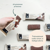 Foodin Clean & Real Protein Bar Crispy Chocolate Bliss; käsi pitelee suorakulmaista Crispy Chocolate Bliss -proteiinipatukkaa metallisessa pakkauksessa, useita samanlaisia patukoita aseteltuna yhtenäiselle valkoiselle taustalle; kääreessä sekä matta- että kiiltäväpintaa lihavoidulla suomenkielisellä tekstillä, joka ilmoittaa 20 grammaa proteiinia ja ei lisättyä sokeria; käsi pitelee patukkaa lisää patukoita esillä valkoisella taustalla, suomenkielinen teksti korostaa proteiini- ja sokerittomuustietoja.