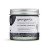 Georganics Aktiivihiili Hammastahna -lasipurkki; pyöreä ja läpinäkyvä purkki mattapintaisella hopeanvärisellä kannella, sisällä tummaa tahnaa; etiketissä lihavoitua ja tavallista tekstausvapaata tekstiä, kuten "naturally fresh breath" ja "100% natural ingredients", sekä mainintoja aktiivihiilestä ja kookosöljystä; kuvattu valkoista taustaa vasten pehmeässä valaistuksessa, ei ihmisiä näkyvissä.
