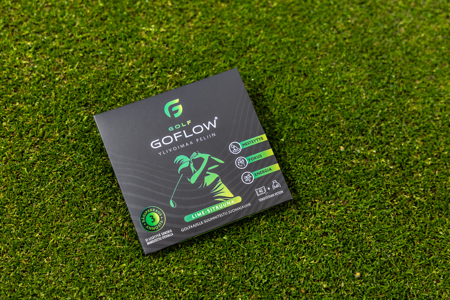 Golf Goflow Mini; musta suorakulmainen rasia tekstillä ”GOFLOW GOLF” ja vihreä golfaajakuvitus aseteltuna tekonurmelle; rasia mattapintainen terävin reunoin; luettavassa tekstissä ”energy”, ”focus” ja ”stamina” yhdessä pienten selkeiden kuvakkeiden kanssa; kirjasin lihavoitu ja groteski; ei ihmisiä tai muita esineitä kuvassa.
