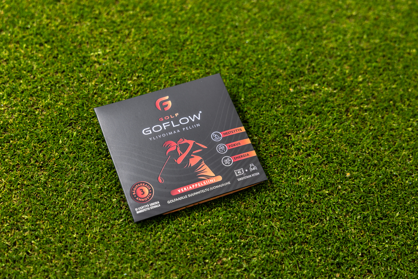 Golf Goflow Pro; GoFlow Golf -tuoterasia golfaajakuvituksella seisoo vihreällä nurmikolla; rasia suorakulmainen pahvia mattapinnalla; pääväreinä valkoinen ja vihreä, lihavoitu groteskikirjasin brändinimessä; luettavassa tekstissä mainitaan liikkuvuus, keskittyminen, energia ja 30 annosta; ei ihmisiä tai käsiä; kamerakulma silmän korkeudelta.