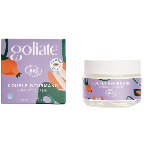 Goliate 2-in-1 Makuliukuvoide Hasselpähkinä; purkki ja rasia Goliaté Couple Gourmand -makuliukuvoidetta, 50 ml, värikkäin hedelmä- ja lehtikuvituksin valkoista taustaa vasten; purkki pyöreä valkoinen rungoltaan yhteensopivalla kierrekannella, pinta kiiltävä; rasia suorakulmainen samaa kuvitusta; tuotenimi lihavoidulla groteskikirjasimella luettavissa molemmissa; studiotyylinen kuva neutraalilla taustalla, ei ihmisiä.