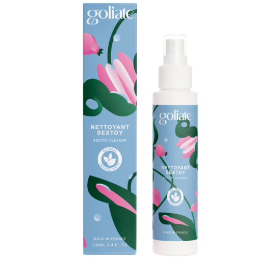 Goliate Seksilelujen Puhdistusaine; pullo ja rasia Goliate Nettoyant Sextoy -puhdistusainetta, molemmissa abstraktia kukkataidetta vaaleanpunaisen, vihreän ja sinisen sävyissä sekä valkoista tuotemerkintää ja hygieniakuvakkeita; pullo sylinterin muotoinen muovia mattapinnalla valkoisella korkilla; rasia suorakulmainen pahvia; etiketissä lukee ”Goliate Nettoyant Sextoy” groteskikirjasimella; vaalea tasainen tausta, ei ihmisiä tai käsiä.