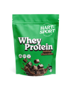 Hart-Sport Whey Protein Suklaa; vihreä mattapintainen pussi Hart-Sport Whey Protein -tuotetta suklaanmaussa; pakkauksessa kuvia suklaapaloista ja nesteroiskeista; 500 g:n pussissa painettuja sertifiointikuvakkeita ja näkyvä heraproteiinibrändäys lihavoidulla groteskikirjasimella; ei ihmisiä tai käsiä kuvassa; tausta tasainen tasaisessa valaistuksessa, tuote kuvan keskellä.