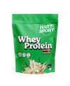 Hart-Sport Whey Protein Vanilja; vihreä pussi Hart-Sport Whey Protein -tuotetta vaniljanmaussa, etusivulla vaniljankukkia ja maitoroiskeita, sisältää 500 g proteiinijauhetta; pussi muovia mattapinnalla, suorakaiteen muotoinen uudelleensuljettavalla yläreunalla; valkoista groteskitypografiaa ja keltaisia tehosteita näkyvissä; tausta tasainen valkoinen; ei ihmisiä tai käsiä; yksittäinen tuote keskitettynä kuvassa.