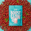 Heey! Boost & Glow Creatine + Coll-egan®, Wild Strawberries: sininen Boost & Glow -lisäravinnepussi mattapinnalla seisoo pystyssä, luettavissa teksti "wild strawberries flavor" ja muuta tuotetietoa modernilla groteskikirjasimella; pussin ympärillä tuoreita kokonaisia metsämansikoita vaaleansinisellä yksivärisellä taustalla; ei ihmisiä tai käsiä näkyvissä, lähikuva tuotteesta.
