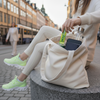 Heey! Energy Sticks Caffeine + Guarana, maku Zesty Citrus; henkilö vaaleissa urheiluvaatteissa istuu kaupunkipuistossa penkillä laittaen energiapatukan valkoiseen kangaskassiin; kassissa älypuhelin, yksinkertaisen kannen muistivihko ja läpinäkyvä vesipullo; kassissa ei näkyviä logoja tai merkintöjä; taustalla rakennuksia ja bussi; ulkona kuvattu laaja otos.