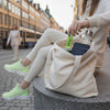 Heey! Energy Sticks Caffeine + Guarana, maku Zesty Citrus; henkilö vaaleissa urheiluvaatteissa istuu kaupunkipuistossa penkillä laittaen energiapatukan valkoiseen kangaskassiin; kassissa älypuhelin, yksinkertaisen kannen muistivihko ja läpinäkyvä vesipullo; kassissa ei näkyviä logoja tai merkintöjä; taustalla rakennuksia ja bussi; ulkona kuvattu laaja otos.