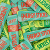 Heey! Energy Sticks Caffeine + Guarana, maku Tropical; kasa suorakaiteen muotoisia mattapintaisia pusseja vihreän ja turkoosin sävyisenä, tekstillä ENERGY STICKS Tropical ja HEY!, limittäin eri suuntiin; ainesosa- ja kofeiinipitoisuustiedot painettu selkeästi etuosaan groteskifontilla; ei ihmisiä tai käsiä; alusta pussien alla ei näkyvissä.