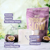 Heey! Hydrate & Glow Electrolytes + Coll-egan® Passionfruit; lasillinen vaaleaa juomaa aseteltuna passionhedelmien ja violetin Hydrate & Glow -pussin väliin; pussi kiiltäväpintainen valkoisin groteskitekstein; näkyvissä olevissa etiketeissä ainesosanimet elektrolyytit, magnesium, vegaaninen kollageeni, koentsyymi Q10, E-vitamiini ja hyaluronihappo; ei ihmisiä tai käsiä; neutraali ja huomaamaton tausta, suoraan edestä kuvattu tuotekuva.