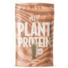 Heey! Plant Protein Peanut Chocolate Caramel; beige ja ruskea pussi, jossa lukee HEEY! PLANT PROTEIN, kuvassa smoothie, 83 % proteiinia -merkintä ja maku Peanut Chocolate Caramel; pakkaus korostaa kasvipohjaista B12-vitamiinia ja vegaanista proteiinipitoisuutta; mattapintainen pussi lohkomaisella valkoisella groteskitekstillä merkin nimessä, lisätekstit ja kuvitus valkoisena ja ruskeana; studiokuva yksivärisellä taustalla, ei ihmisiä tai rekvisiittaa näkyvissä.