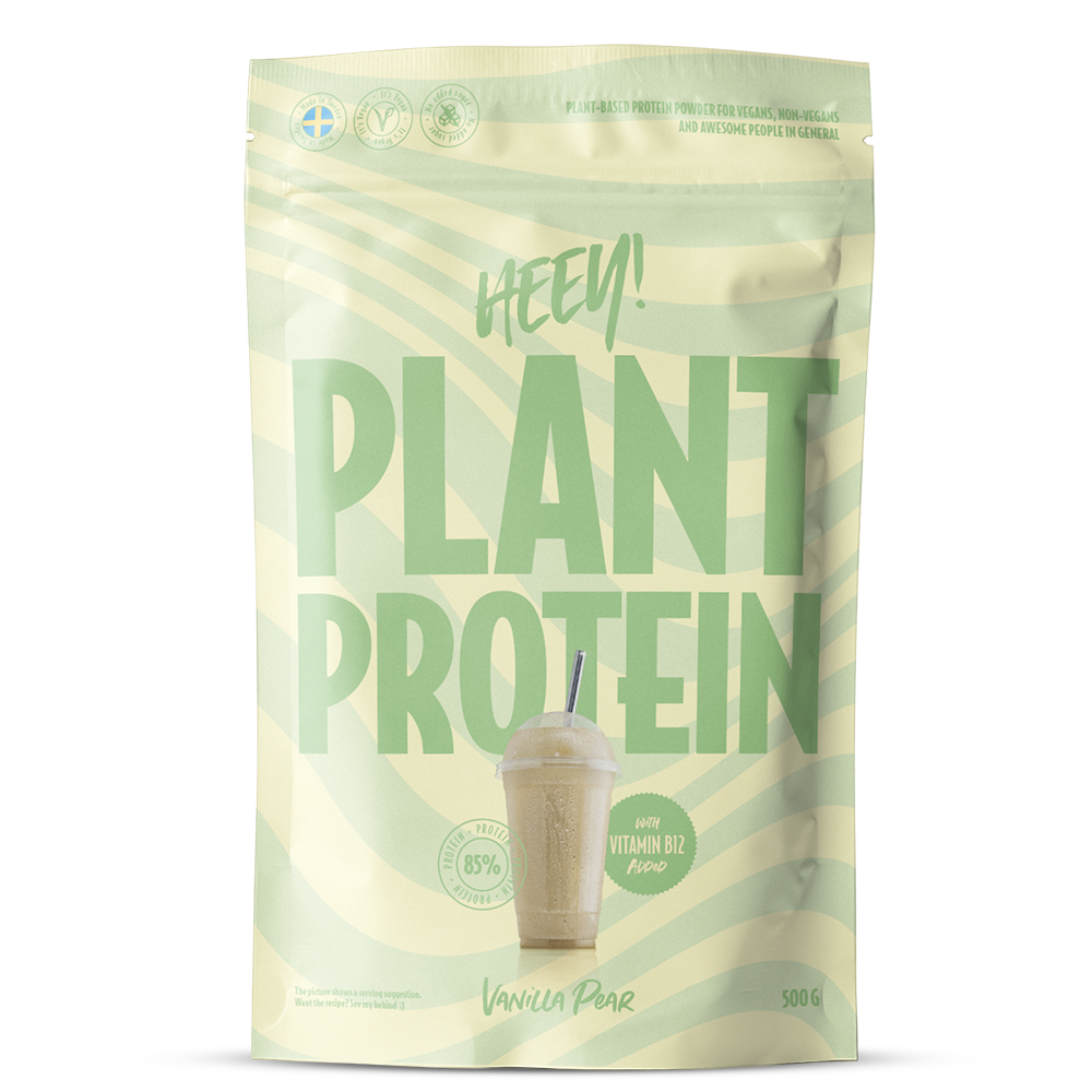 Heey! Plant Protein, maku Vanilla-Pear; vaaleanvihreä pussi tekstillä HEEY! PLANT PROTEIN, kuva vanilja-päärynäshakesta pillin kera; mattapintainen joustava materiaali, suorakaiteen muotoinen pohja, lämpösaumatut reunat; lihavoitu groteskityypografia valkoisena ja mustana; etuteksti mainitsee 85 % kasviproteiinia, B12-vitamiinia ja 500 g; ei ihmisiä tai käsiä; vaalea tausta, tuote pystyssä suoraviivaisessa studiokuvassa.