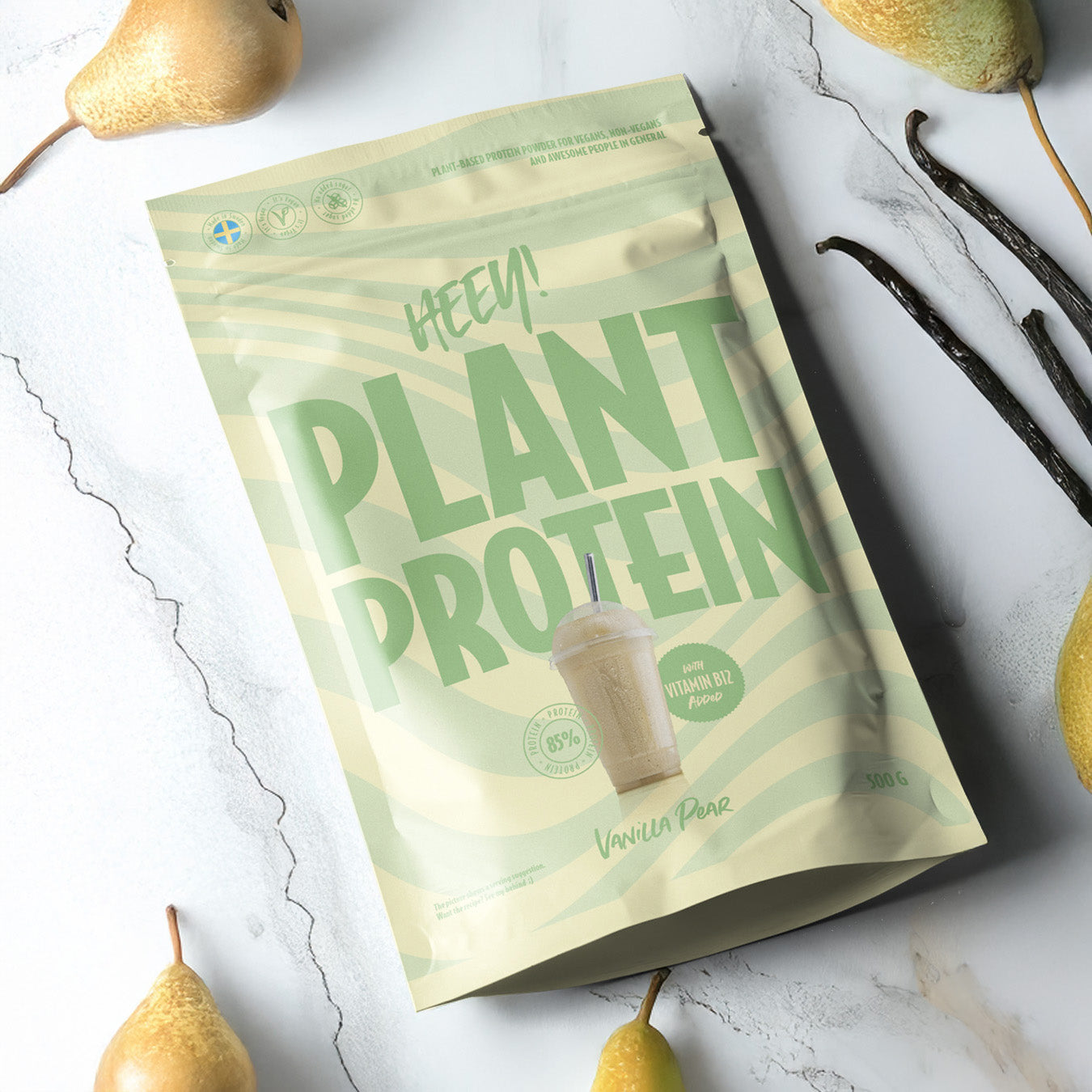Heey! Plant Protein, maku Vanilla-Pear; beige-vihreä pussi tekstillä PLANT PROTEIN Vanilla Pear, kuva smoothiesta, marmoripinnalla tuoreiden päärynöiden ympäröimänä, korostaen kasvipohjaista proteiiniseosta; pakkaus mattapintainen, suorakaiteen muotoinen ja pystyssä; etiketissä lihavoitu groteskiteksti tuotenimelle; ei ihmisiä tai käsiä kuvassa.
