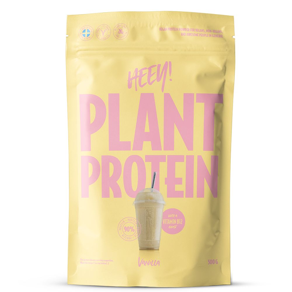 Heey! Plant Protein Vanilla; keltainen pussi, jossa lukee PLANT PROTEIN, kuvassa vaniljamakuinen proteiinijuoma, pinkkiä tekstiä ja symboleja, sisältää 500 g kasvipohjaista proteiinijauhetta vaniljan maulla; muovipakkaus on mattapintainen, suorakulmainen suljetulla yläreunalla; pääetiketissä lihava groteskikirjasin pinkkinä ja valkoisena; pussi seisoo pystyssä vaaleaa taustaa vasten, ei ihmisiä tai käsiä näkyvissä.