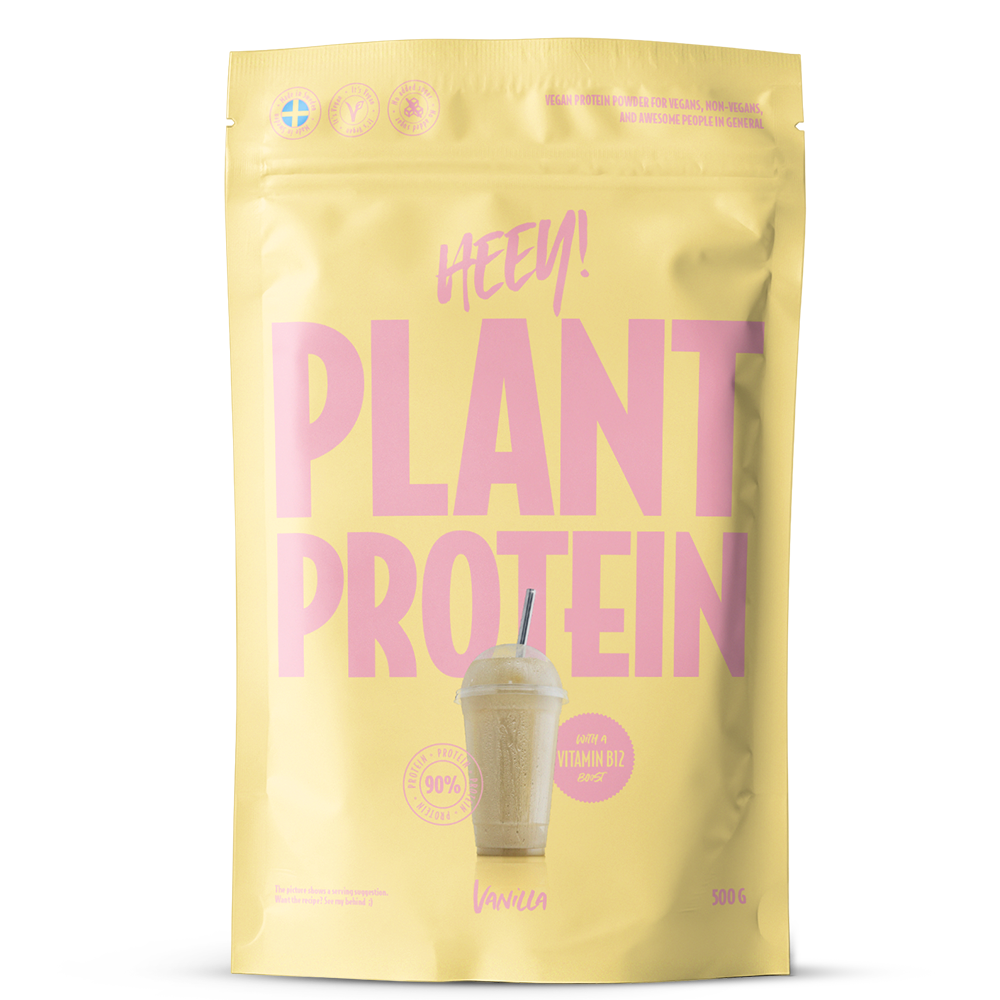 Heey! Plant Protein Vanilla; keltainen pussi, jossa lukee PLANT PROTEIN, kuvassa vaniljamakuinen proteiinijuoma, pinkkiä tekstiä ja symboleja, sisältää 500 g kasvipohjaista proteiinijauhetta vaniljan maulla; muovipakkaus on mattapintainen, suorakulmainen suljetulla yläreunalla; pääetiketissä lihava groteskikirjasin pinkkinä ja valkoisena; pussi seisoo pystyssä vaaleaa taustaa vasten, ei ihmisiä tai käsiä näkyvissä.