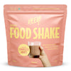 Heey! Vegan Food Shake, maku Chocolate; vaaleanpunainen mattapussi tekstillä Heey! Food Shake, pystyssä, etuosassa painettu kuva lasista tummanruskeaa suklaisen shaken näköistä nestettä; suurta ja pienempää valkoista groteskitekstiä etuosassa; avainlauseita plant-based, complete meals, 25 vitamins ja 35g protein; vaalea tausta, ei ihmisiä tai lisärekvisiittaa kuvassa.