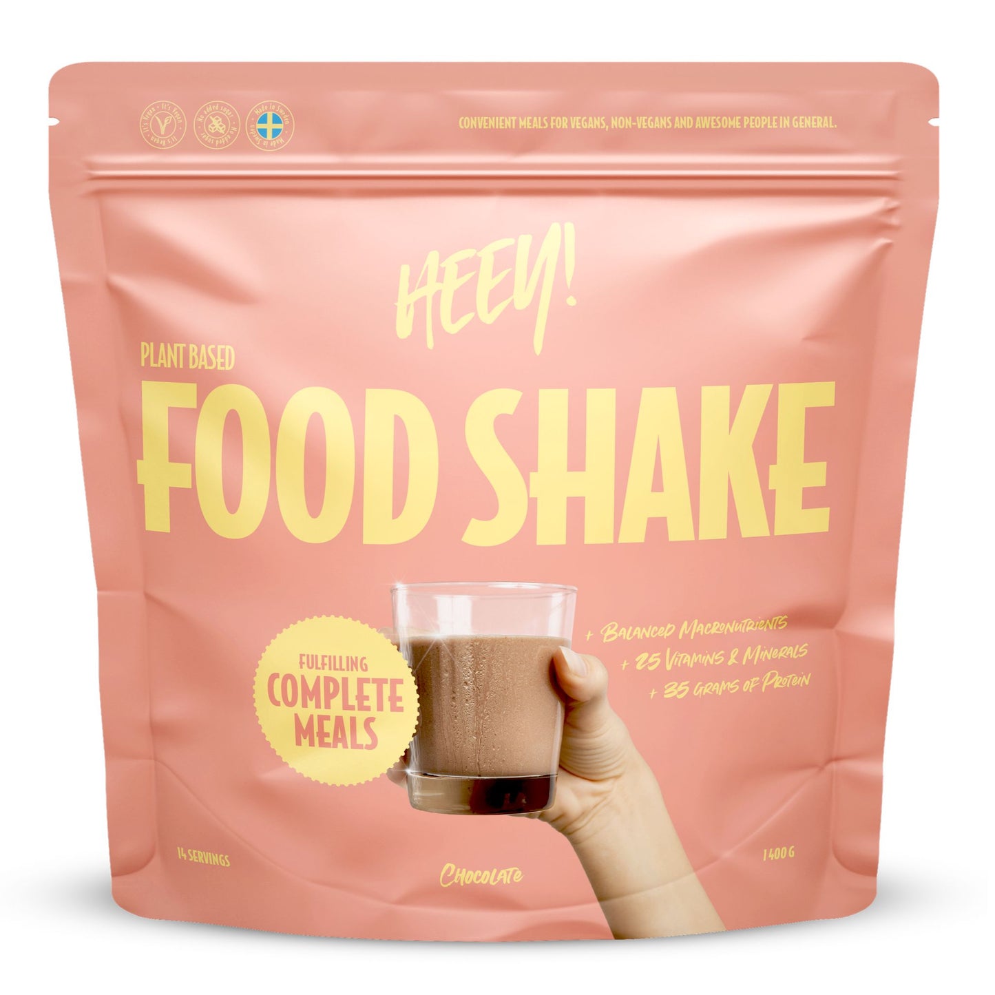 Heey! Vegan Food Shake, maku Chocolate; vaaleanpunainen mattapussi tekstillä Heey! Food Shake, pystyssä, etuosassa painettu kuva lasista tummanruskeaa suklaisen shaken näköistä nestettä; suurta ja pienempää valkoista groteskitekstiä etuosassa; avainlauseita plant-based, complete meals, 25 vitamins ja 35g protein; vaalea tausta, ei ihmisiä tai lisärekvisiittaa kuvassa.