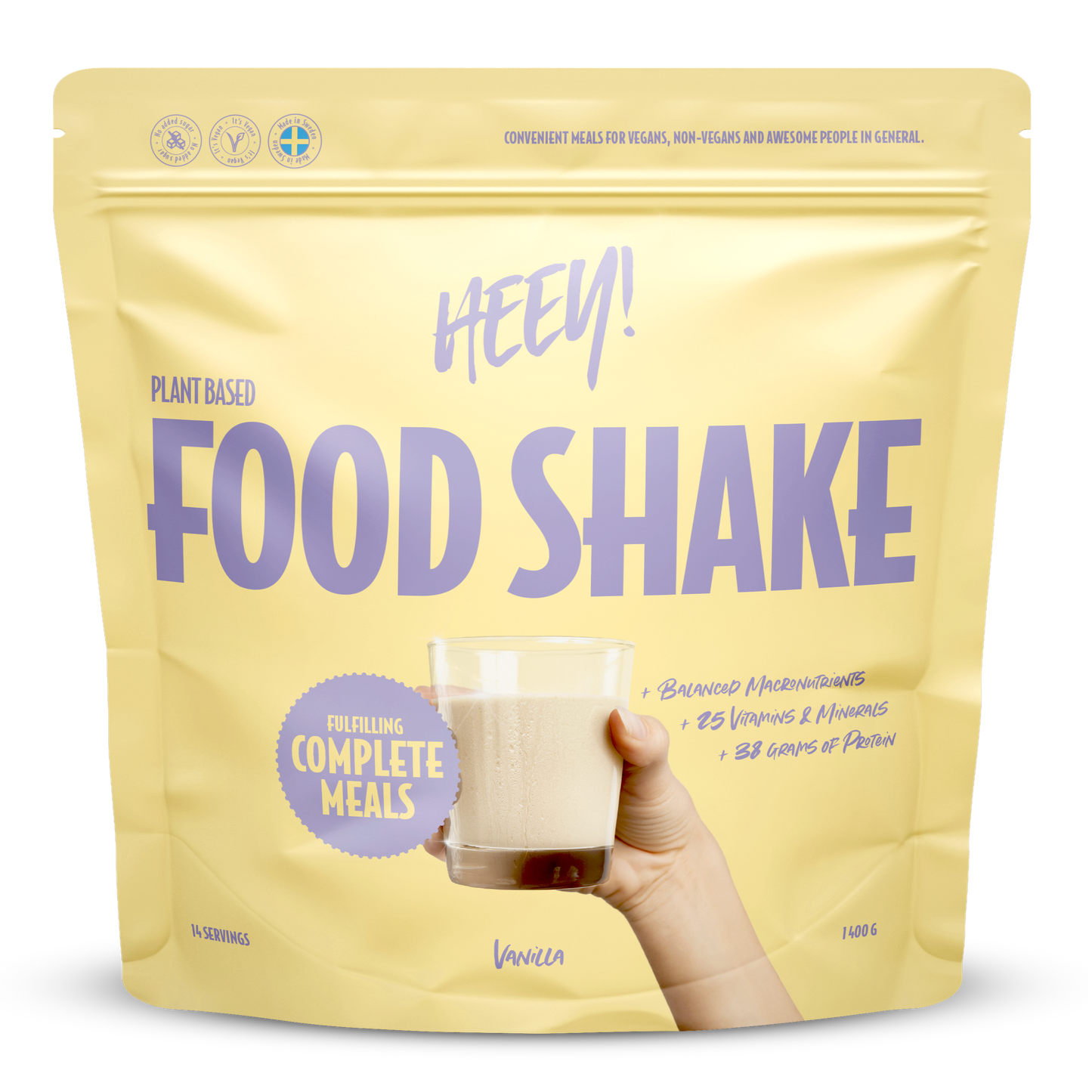 Heey! Vegan Food Shake, maku Vanilla; keltainen mattapintainen pussi tekstillä Heey! Food Shake pystyssä tasaisella alustalla; lihavoitua valkoista ja mustaa groteskitypografiaa, etiketissä complete meals, 25 vitamins & minerals ja 33g protein; ihmiskäsi pitelee kirkasta lasillista vaaleaa vanilja-shaketta pussin vieressä; tausta ei näytä yksityiskohtia.