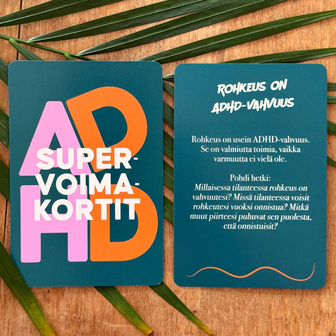 Hidasta Elämää ADHD-supervoimakortit: kaksi värikästä korttia lepää puupinnalla vihreiden lehtien koristelemana; toisen otsikko on "ADHD SUPERVOIMAKORTIT", toinen kertoo suomeksi ADHD:n vahvuuksista rohkaisten pohtimaan hetkiä, jolloin rohkeudesta tulee ADHD:n supervoima; kortit ovat suorakulmaisia pyöristetyin kulmin ja mattapintaisia; typografia on selkeää ja lihavoitua molemmissa korteissa; ei ihmisiä tai käsiä näkyvissä.