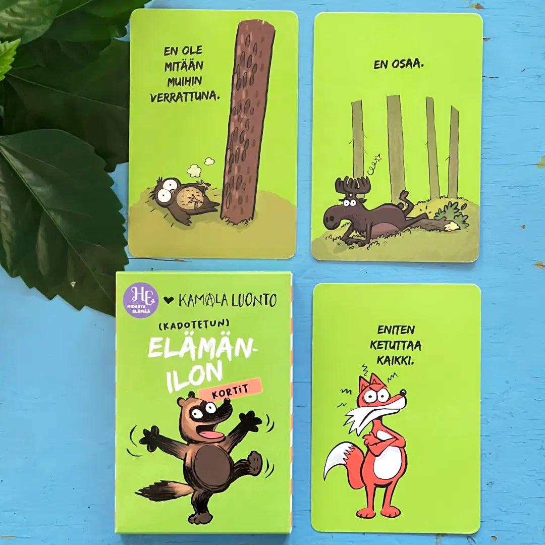 Four illustrated cards with Finnish text; animals include a bear hugging a tree, a moose among trees, a happy squirrel, and an annoyed fox holding up a paw. All cards feature bright green backgrounds and charming wildlife details. The cards are rectangular, printed on matte cardstock with smooth edges. Text is in black sans-serif font centered near the top of each card. Cards are unboxed and positioned side by side on a white surface in top-down view. No people or hands are present in the image.