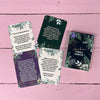 Four Finnish-language cards with floral borders are displayed on a pink wooden surface next to a rectangular Herään Voima-Kortit box. The box has a glossy finish, decorated with green leaves and flowers, and features serif text. No people or hands are visible in this tabletop product shot.