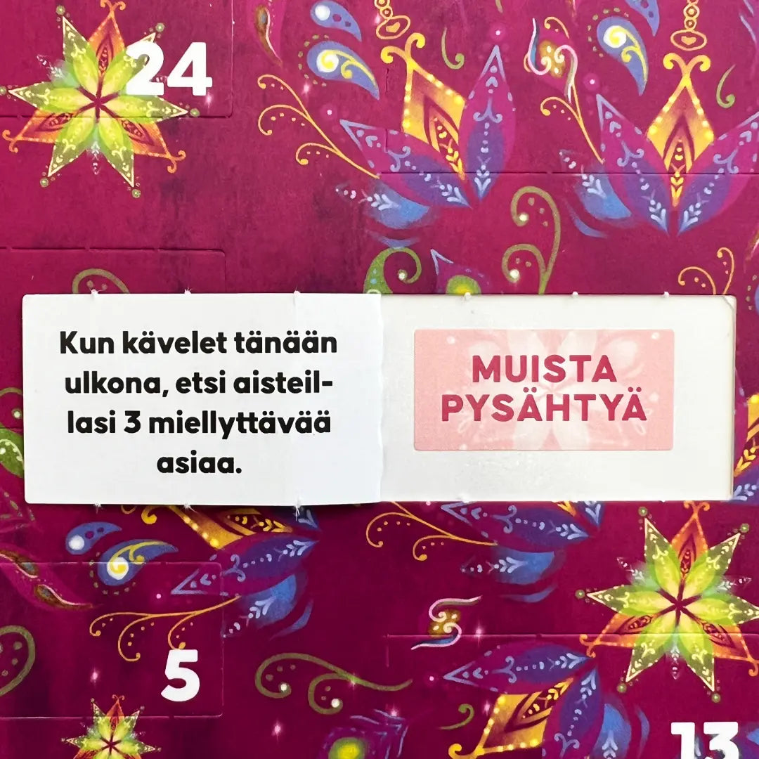 Hidasta Elämää Onnenhetkien Joulukalenteri; värikäs kalenteri, jossa näkyvissä numerot 24, 5 ja 13; lihavoidut numerot mattapintaisilla, eri muotoisilla ja värisillä pahviluukuilla; yksi luukku avattuna paljastaa suomenkielisen tekstin: Kun kävelet tänään ulkona, etsi aisteillasi 3 miellyttävää asiaa. MUISTA PYSÄHTYÄ; suorakaiteen muotoinen asettelu, neutraali tausta, ei käsiä tai muita esineitä.