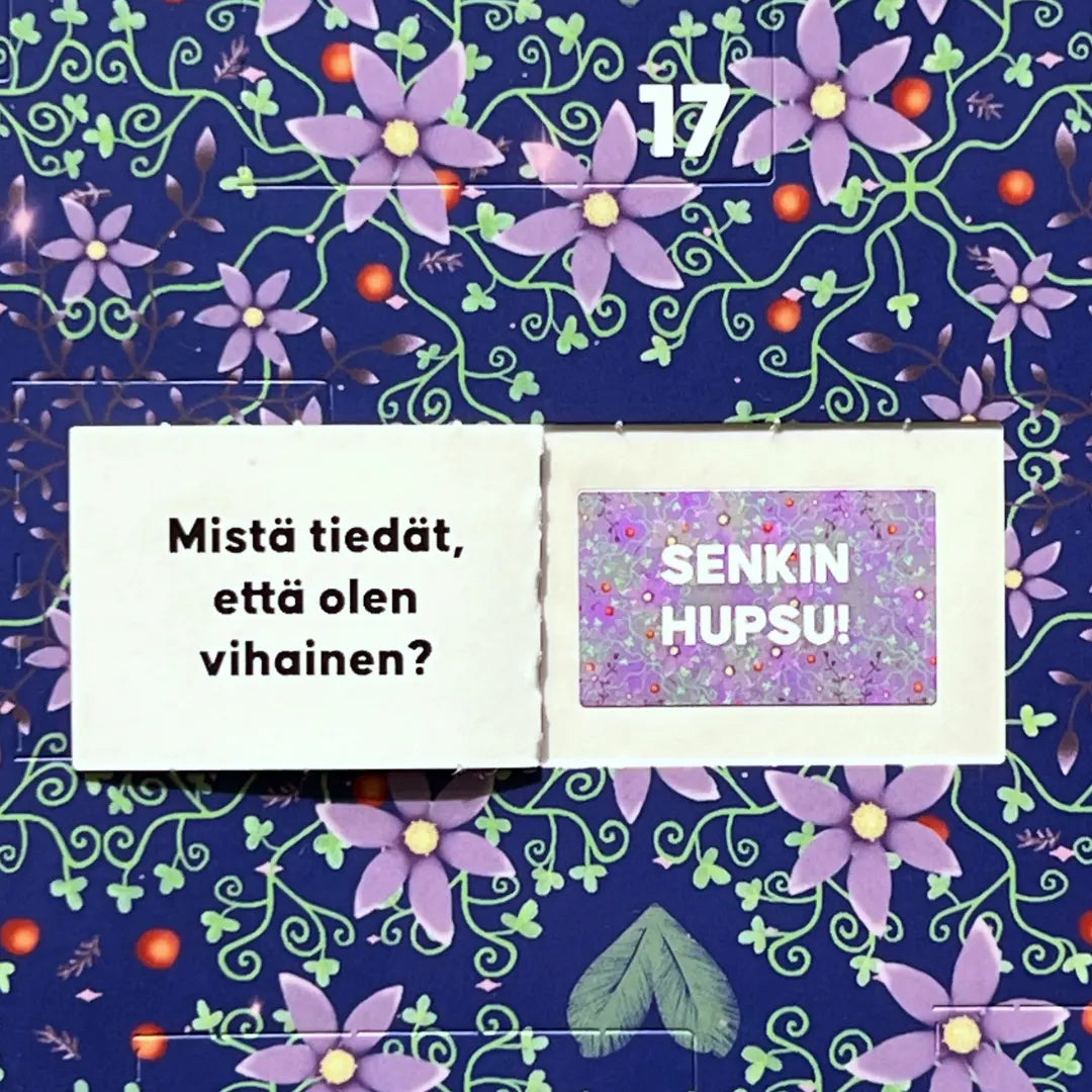 Hidasta Elämää Paremman Parisuhteen Joulukalenteri; luukku numero 17 avattuna paljastaa suomenkielisen tekstin Mistä tiedät, että olen vihainen? ja SENKIN HUPSU! värikkäällä violetti-vihreällä kukkataustalla; kalenteri suorakaiteen muotoinen, kiiltäväpintainen paperi; lihavoitu valkoinen groteskifontti; ei pakkausta, ihmisiä tai muuta ympäristöä näkyvissä.