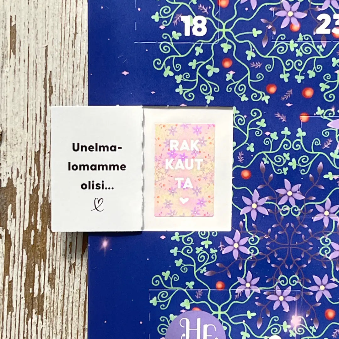 Hidasta Elämää Paremman Parisuhteen Joulukalenteri; avattu kalenteriluukku paljastaa suomenkielisen tekstin ja pinkin, tähdillä koristellun kortin, jossa lukee RAKKAUTTA sekä sydämiä, sinis-violetilla kukkataustalla; luukut suorakaiteen muotoisia, kiiltäväpintaisia; vaalealla puualustalla, ei ihmisiä; kuvakulma yläviistosta.