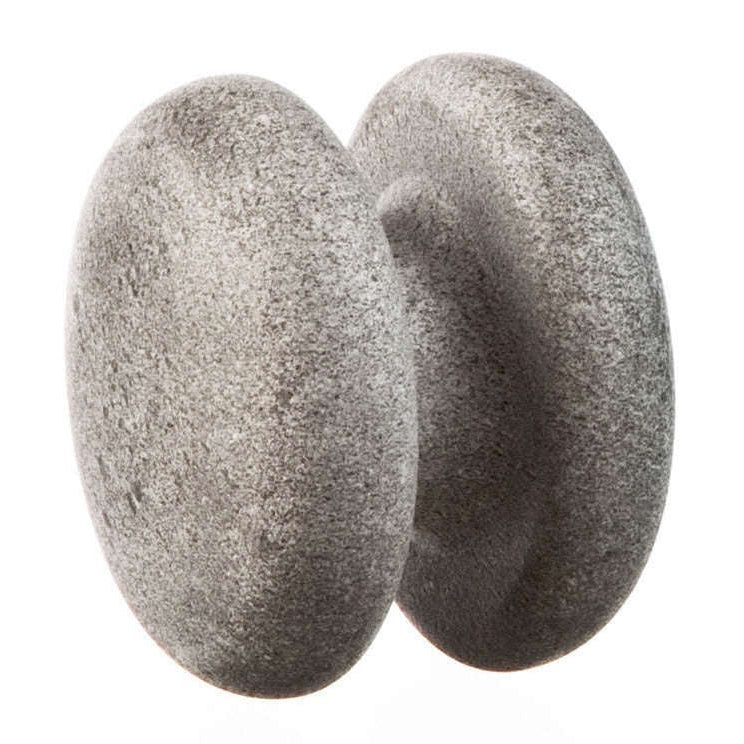 Two smooth, round gray stones are balanced upright and pressed together, creating a narrow gap between them against a white background. The stones have a matte finish and no visible markings or labels. No packaging is present. The image uses even lighting with no shadows, showing only the stones without people or additional objects in frame.