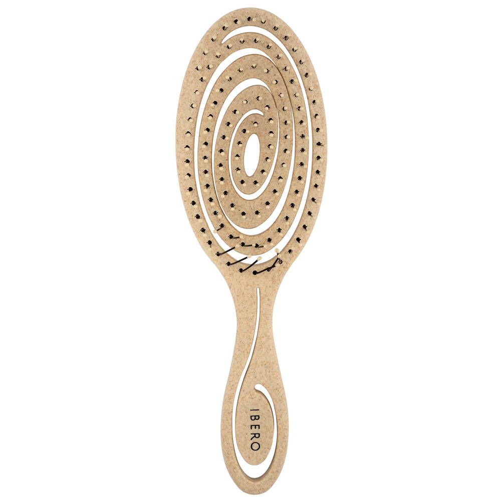 A beige, vented hairbrush with an oval shape and spiral-patterned bristles is positioned on a white background. The handle is matte and printed in uppercase letters with the word “IBERO” in black. No packaging or additional elements are visible, and the image is an overhead shot of the brush alone.