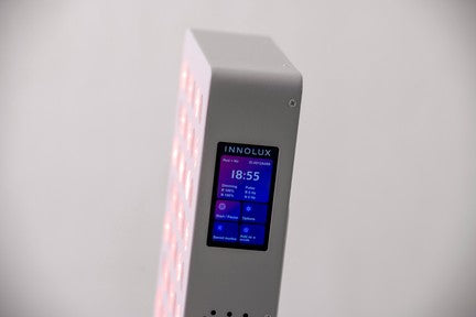 Innolux RED S2 PRO Punavalo; lähikuva suorakaiteen muotoisesta laitteesta digitaalisella näytöllä, joka näyttää tekstin ”INNOLUX” ja asetuksia; laite mattapintainen, pääosin valkoinen tai vaaleasävyinen, toisella puolella näkyvissä himmeä punaisten LED-valojen ruudukko; näytön teksti yksinkertaisella tikkukirjasimella; tausta tasainen valkoinen, ei pakkausta, ihmisiä tai muita esineitä näkyvissä.