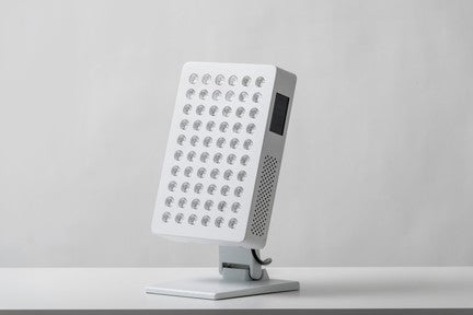 Innolux RED S2 PRO Punavalo; suorakaiteen muotoinen valkoinen LED-paneelivalo useine pyöreine lamppuineen, kiinnitettynä suoraan metalliseen jalustaan, lepää sileällä mattavalkoisella pinnalla ilman näkyvää pakkausta tai etikettejä; lamput tasavälein paneelissa; ei näkyvää typografiaa; tausta tasainen vaaleanharmaa; ei ihmisiä tai käsiä näkyvissä; suorakaiteen muotoinen LED-paneelivalo jalustallaan säteilee kirkasta valaistusta.