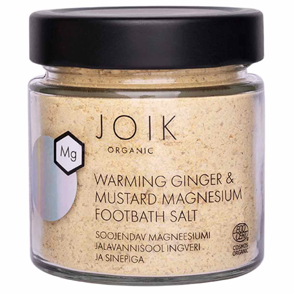 JOIK Organic Warming Magnesium Jalkakylpysuola; lasipurkki, merkitty JOIK Organic Warming Ginger & Mustard Magnesium Footbath Salt, mustalla kannella, sisältää vaaleankeltaista magnesiumpitoista kylpysuolaa; purkki on läpinäkyvä ja sylinterinmuotoinen kiiltävällä mustalla kierrekorkilla; etiketti on valkoinen vähäisellä mustalla groteskitekstillä; ei ihmisiä, käsiä tai rekvisiittaa näkyvissä; tuote on ainoa esine kuvassa yksivärista taustaa vasten keskitetysti kuvattuna.
