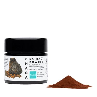A jar labeled Chaga Extract Powder sits next to a small mound of brown powder. The cylindrical jar has a matte label showing an illustration of a Chaga mushroom and includes the words “Chaga Extract Powder” with additional text mentioning adaptogenic properties. The background is plain and white, and no people or hands are present in the image.