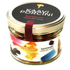 A glass jar of Kaayni brand dried chanterelle mushrooms, labeled kanttarelli cantharellus cibarius. The jar is cylindrical and transparent with a glossy black lid bordered by a silver metallic rim. The label has yellow, blue, and black brushstrokes on white and includes product names in clear sans-serif font. Studio setting with a plain background.