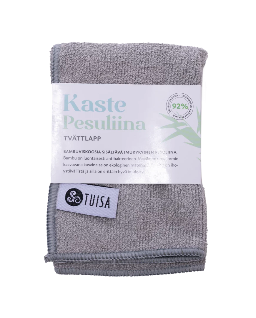 Kaste Pesuliina, taitettu harmaa pesuliina valkoisella suomenkielisellä etiketillä, jossa vihreitä yksityiskohtia ja TUISIA-tunnus; kankaan pinta mattaa, materiaali keskipaksua; etiketissä siistiä groteskitekstiä, joka mainitsee bambukuidut; ei pakkausta tai muita taustaelementtejä kuin pelkkä valkoinen tausta; ei ihmisiä eikä toimintaa näkyvissä.